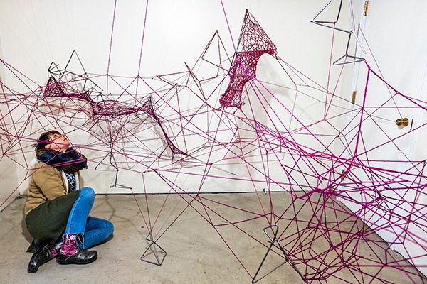 Student peers at a sculpture made of steel and bright pink yarn