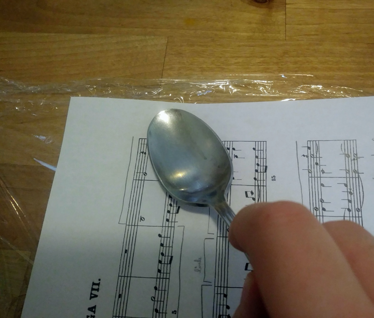 Using a spoon to press paper onto plastic wrap