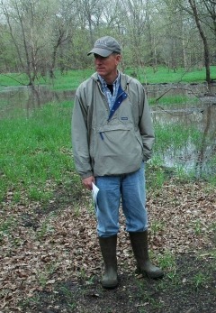 Keith Schilling standing in a wooded area observing nearby river water.