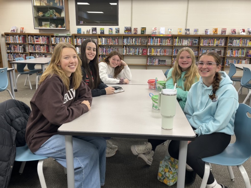 A group of young women sit around a school cafeteria table
