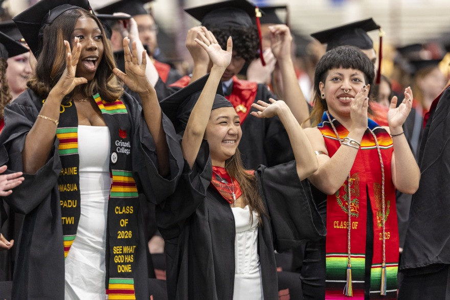 Students wearing black graduation gowns and caps standing and applauding