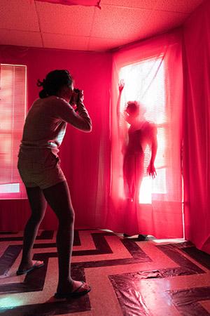 One student photographs another in a red-draped room with black chevron design on the floor