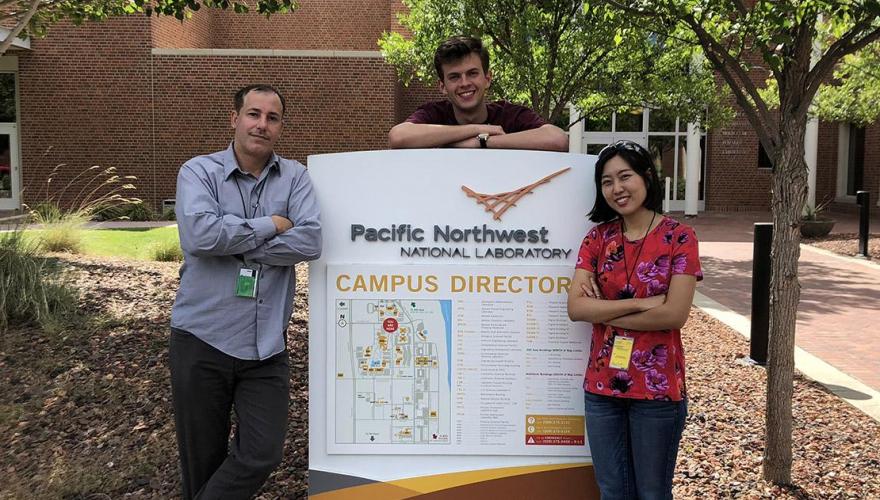 Two research students with their faculty mentor, Prof. Hernandez, leaning on a campus sign at the Pacific Northwest National Laboratory.