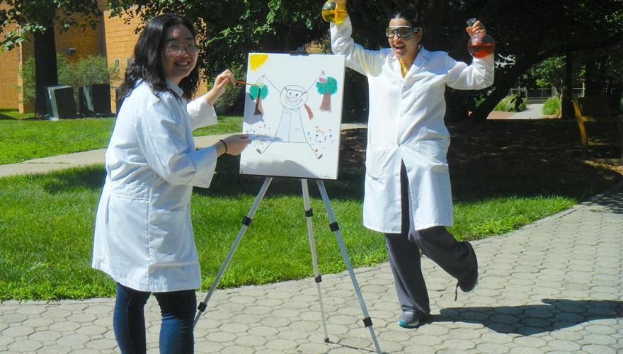 A research student with their faculty mentor, Prof. Ortiz, wear lab coats and hold glass flasks.