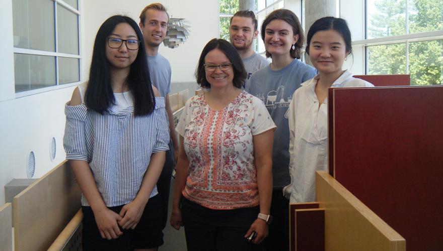 Five students and their faculty mentor among the study carrels in the science library.