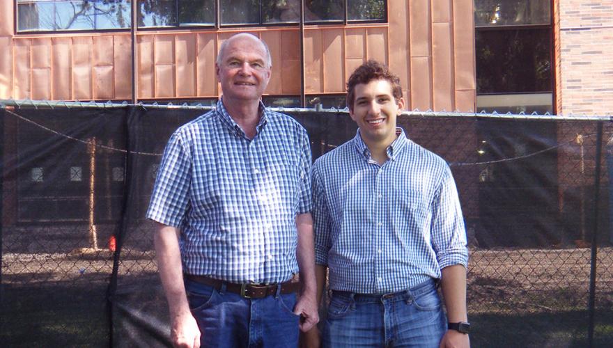 A student and his faculty mentor stand in front of the copper facade of a building.