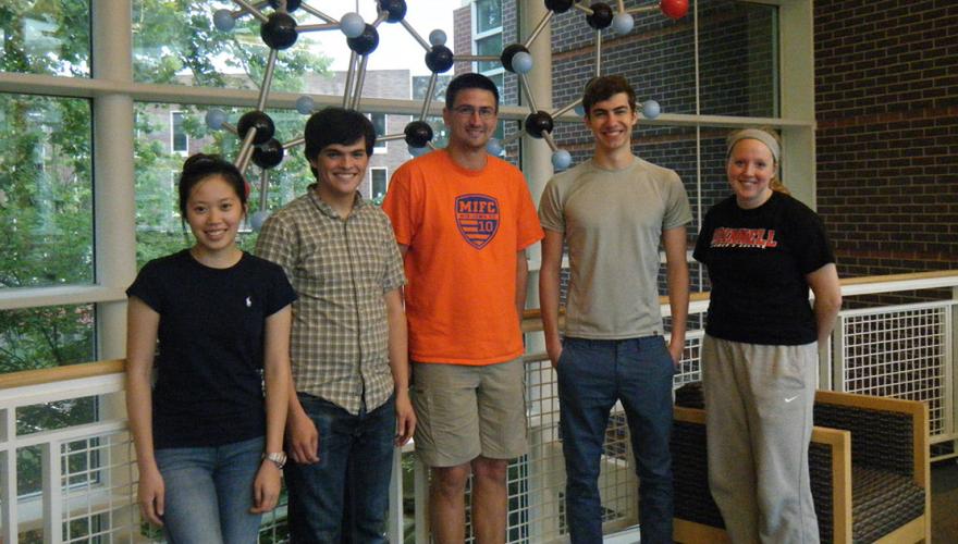 Four students and their faculty mentor stand in front of a large molecule sculpture.