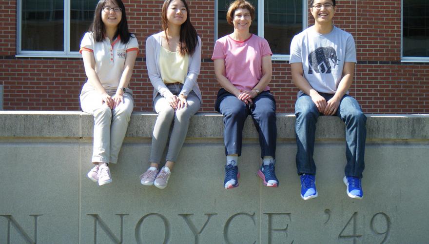 Three students and their faculty mentor sit on a low wall.