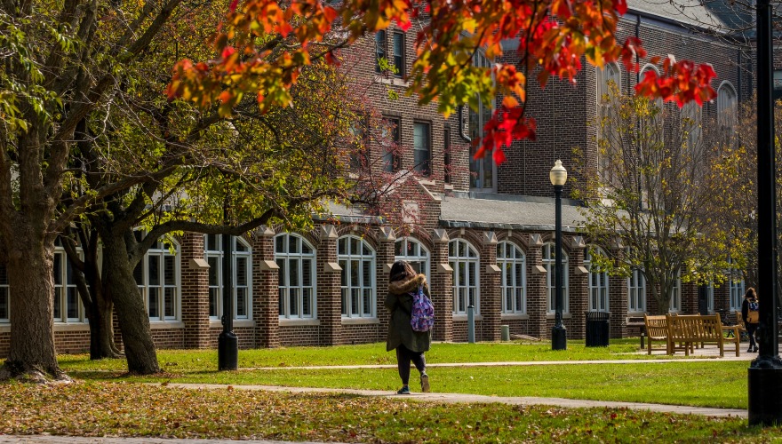 Student walks on campus with colorful leaves in the fall