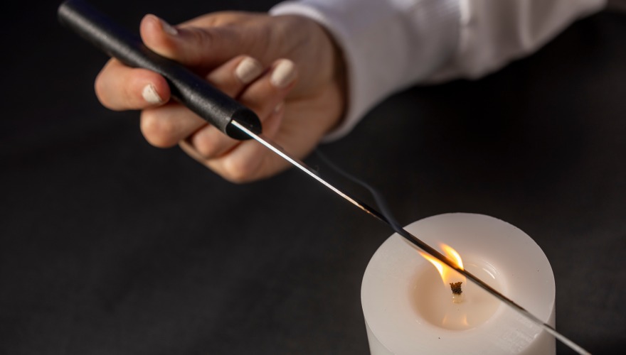 A hand holds a knife over a candle's flame.