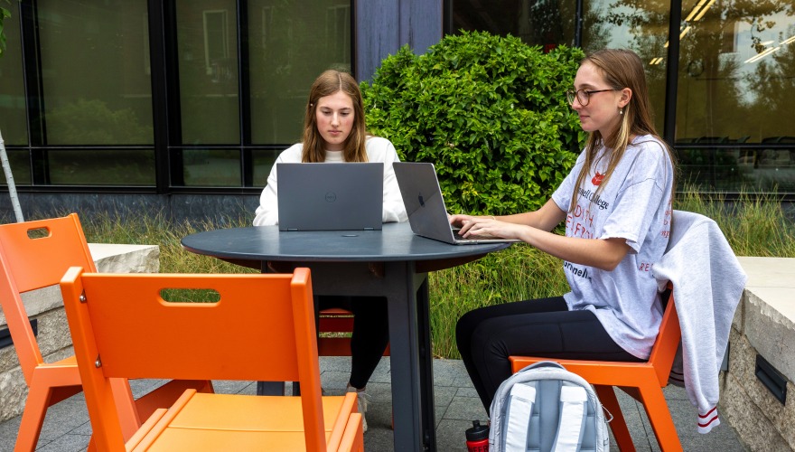 Strovers (left) and Ford (right) sit at a table outside the HSSC and type on their computers.