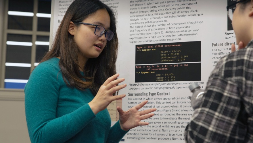 A young woman stands next to a poster and explains her research to a fellow student.