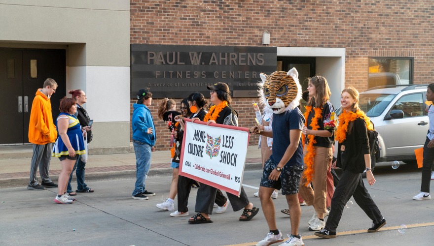 people walking in pararde carrying a sign that says more culture less shock, one wears a tiger mascot head