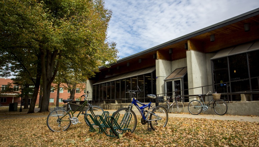 A picture of the Wellness Center forum in the fall. A bunch of leaves on the ground by a bicycle rack in front of the forum doors.