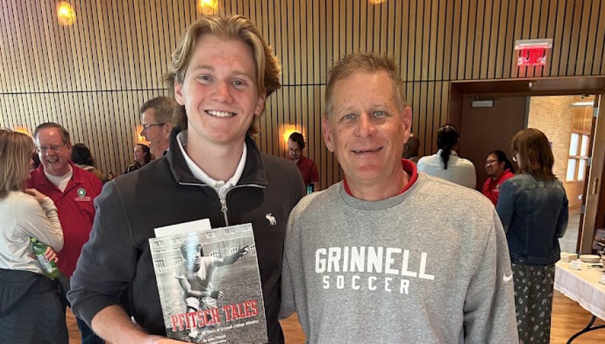A smiling young man holds an award, standing alongside another man