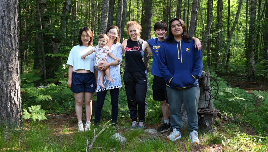 The student researchers and their professor (holding her baby) pose for a group photo in the woods