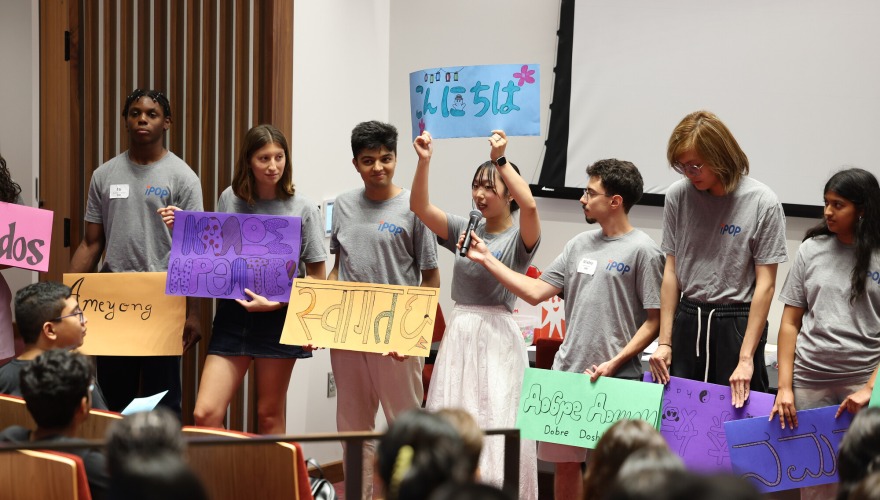 Seven students wearing gray shirts standing in a line and holding colorful signs.