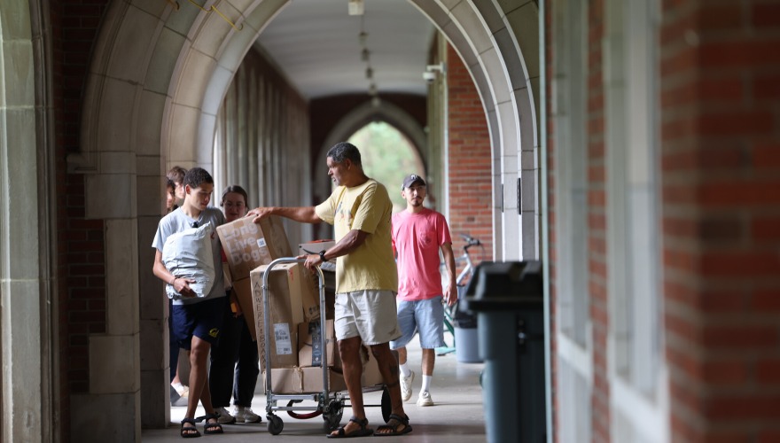 A small group of people putting boxes on a cart under an arched loggia.