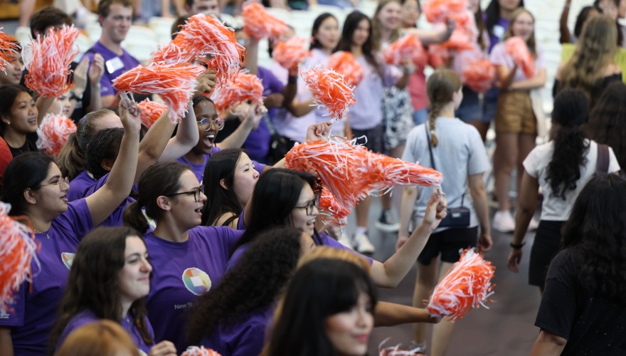 A large group of students cheer and wave red and white pompoms.