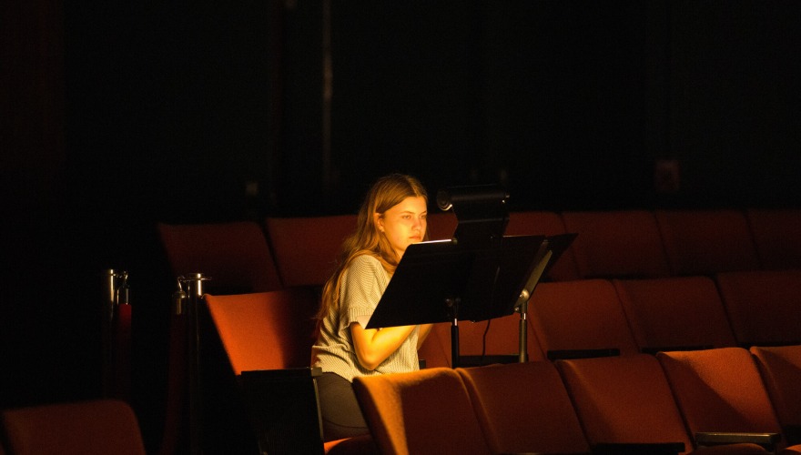 A student sitting in an empty auditorium lit by a small lap