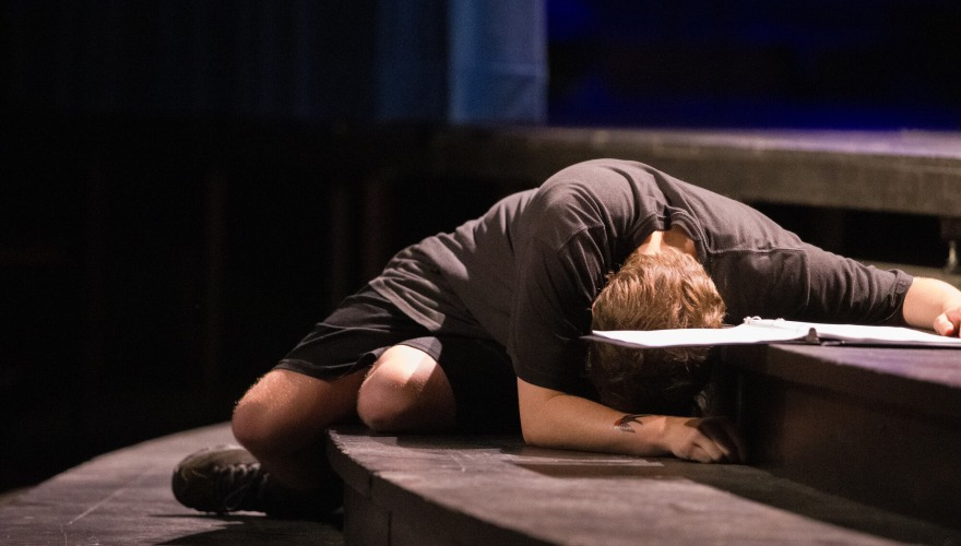 A student in black laying on stage steps with their head down