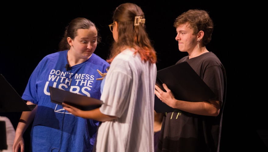 Three students standing on a dark stage holding black binders