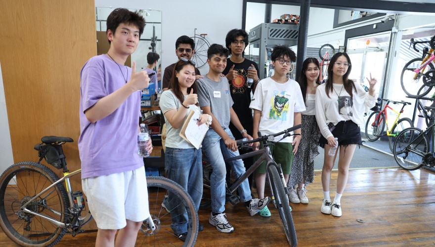 A group of international students stand around an IPOP mentor sitting on a bicycle.
