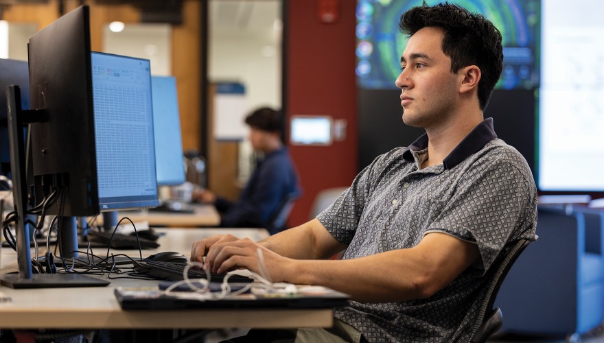 Alex Stein works at a keyboard in front of a couple of monitors. 