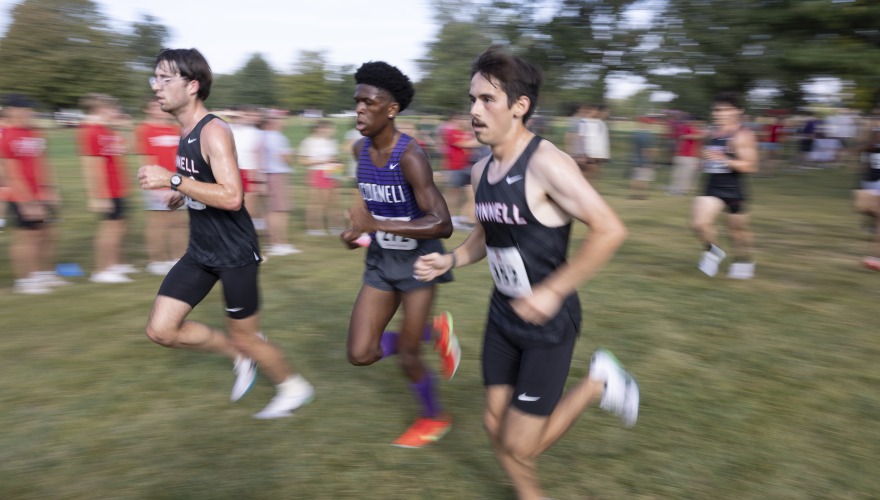 Three male college students wearing cross country uniforms running together