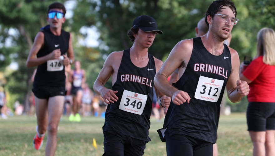 Three male college students wearing cross country uniforms and race bibs running one after another