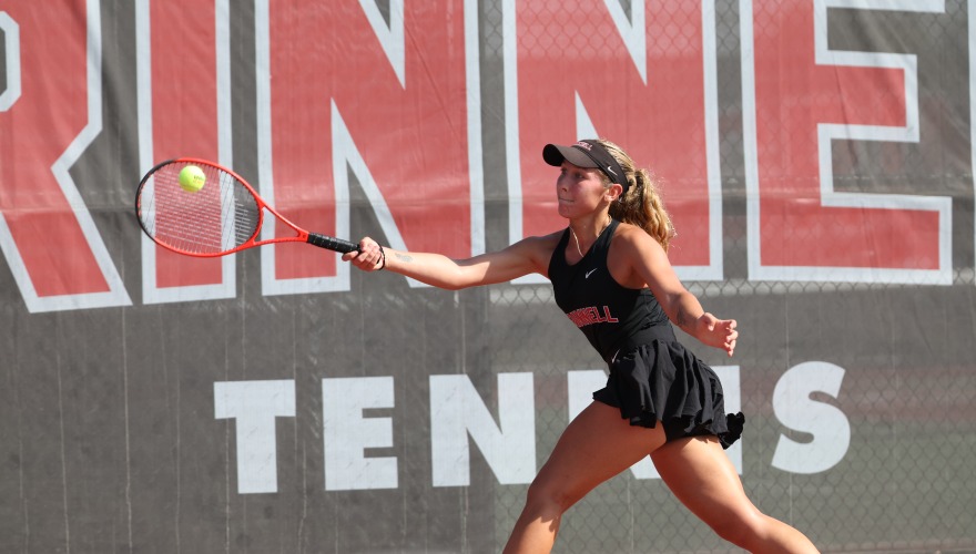 A college tennis player reaches to hit a tennis ball with a red racket 
