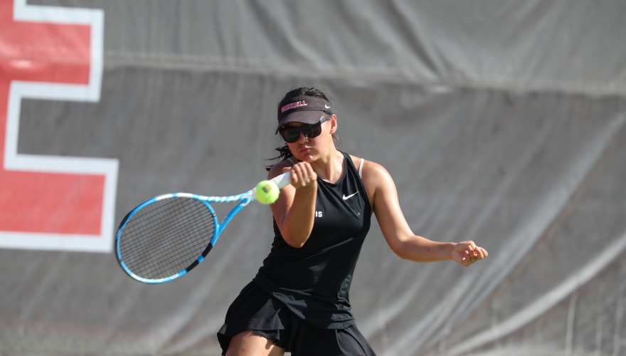 A college tennis player lined up to hit a tennis ball with a blue racket 