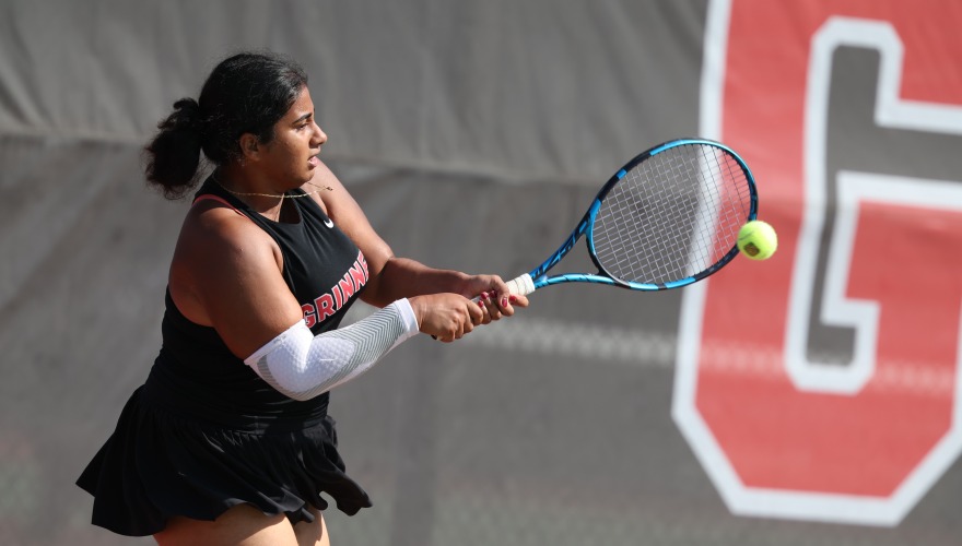 A college tennis player reaches to hit a tennis ball with a blue racket 