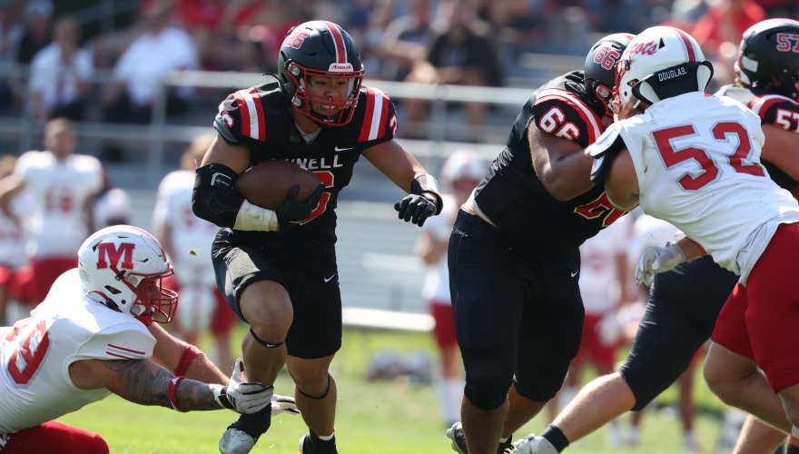 A football player in black runs the ball past defenders in white and red