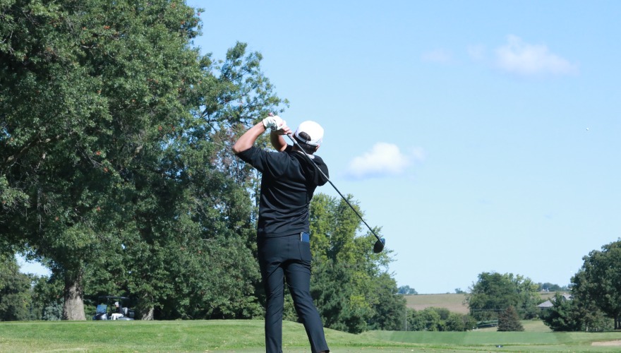 A golfer in black stands in follow through looking at the shot he just took