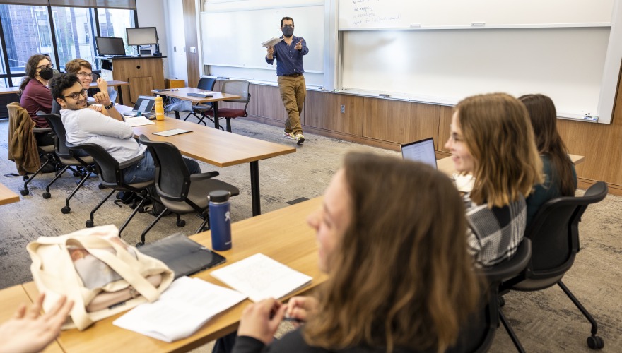 A teacher stands at the front a classroom, leading a discussion