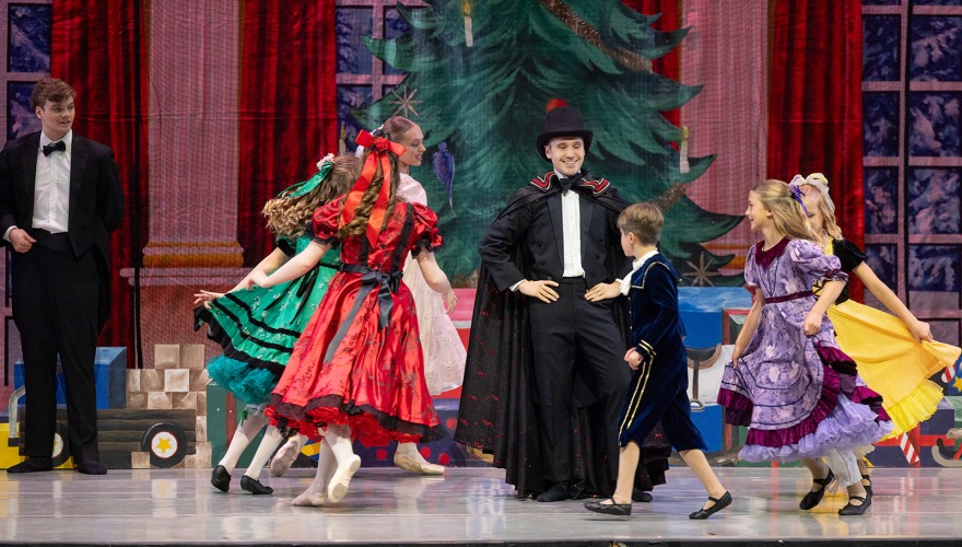 2 adults and children dancing on stage with a Christmas tree in the background