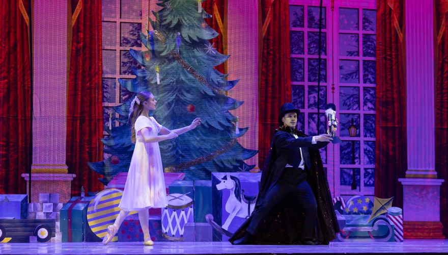 Girl and boy on stage doing ballet with Christmas tree in background