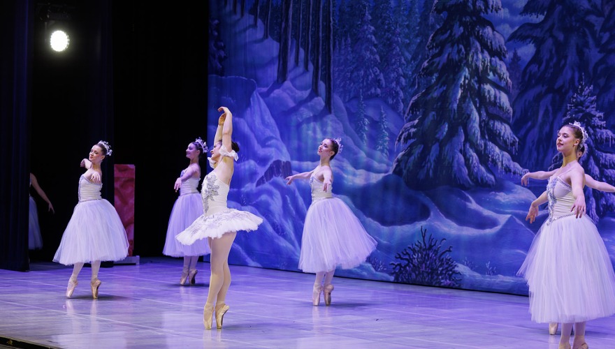 dark snow scene on stage with girls in white dressing doing ballet