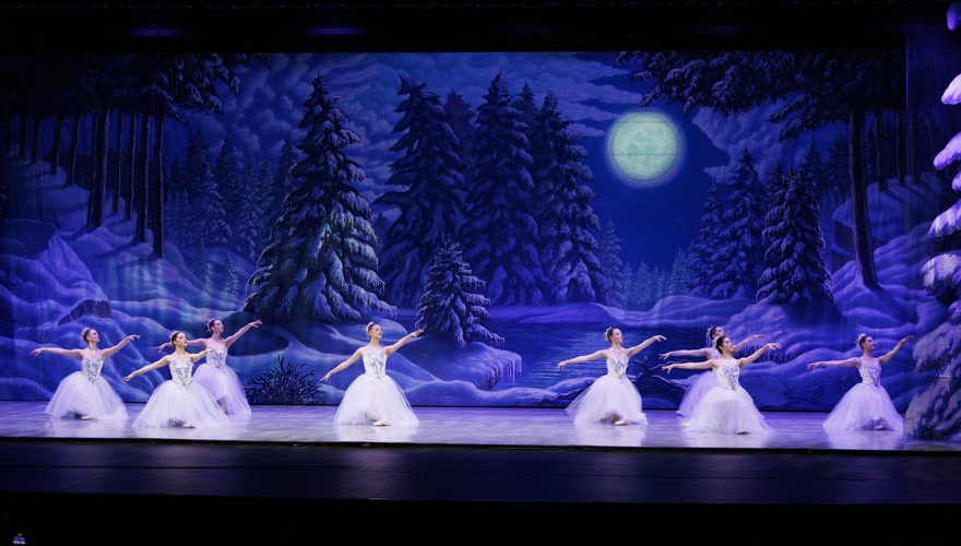 dark snow scene on stage with girls in white dressing doing ballet