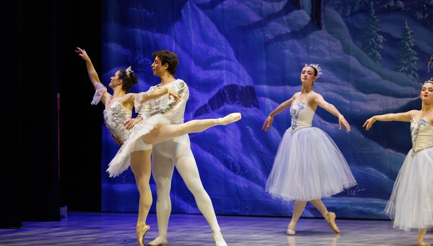 dark snow scene on stage with a man and a woman in white dancing ballet