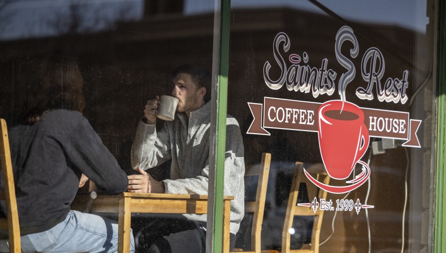 A view of Saints REst Coffee House through the front window. Two young people sip coffee at a table.