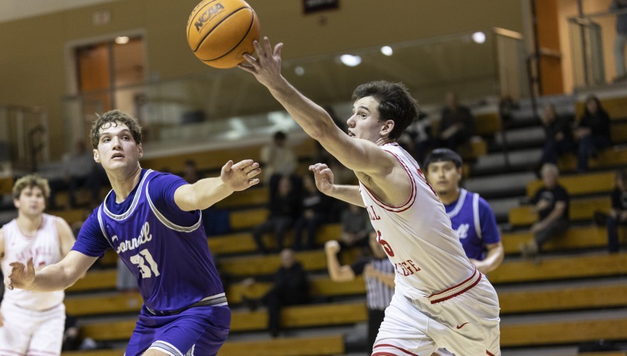 A basketball player wearing a white Grinnell uniform reaches for the ball in front of two defending players in purple