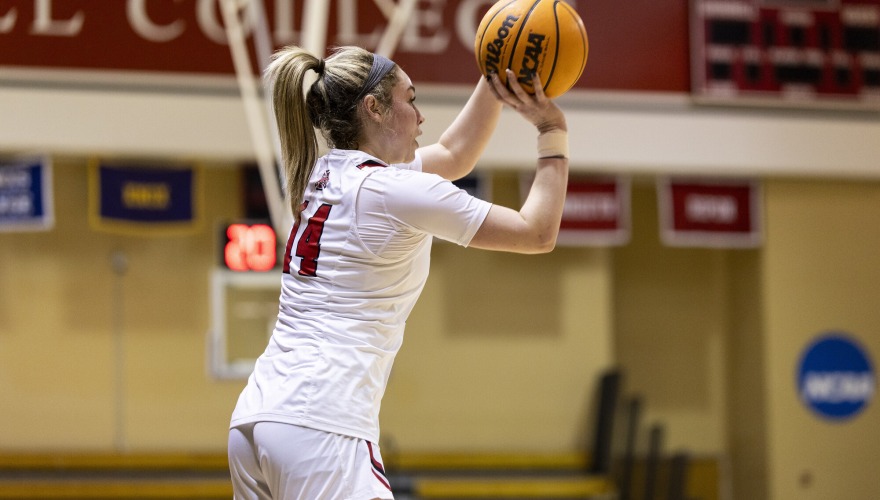 A basketball player with her hair in a blonde ponytail and wearing a white Grinnell uniform shoots the ball