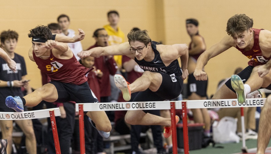 Three students in red and black track uniforms leaping over hurdles
