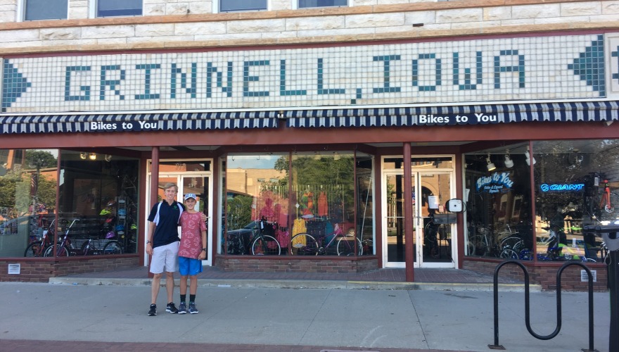 James at 14 poses with his brother Daniel in downtown Grinnell in front of a vintage storefront sign that says "Grinnell, Iowa"