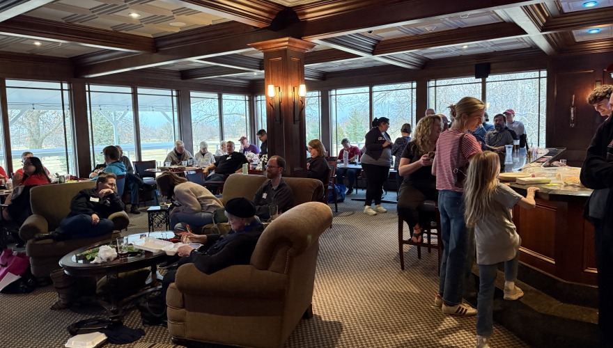 A large group of people sitting in chairs scattered around a warm, carpeted room