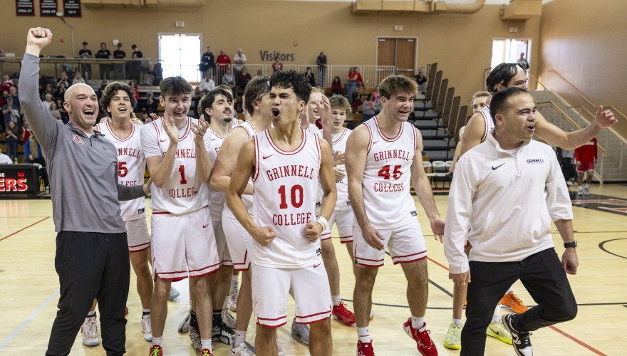 Men's basketball players wearing white uniforms walking excitedly off the court