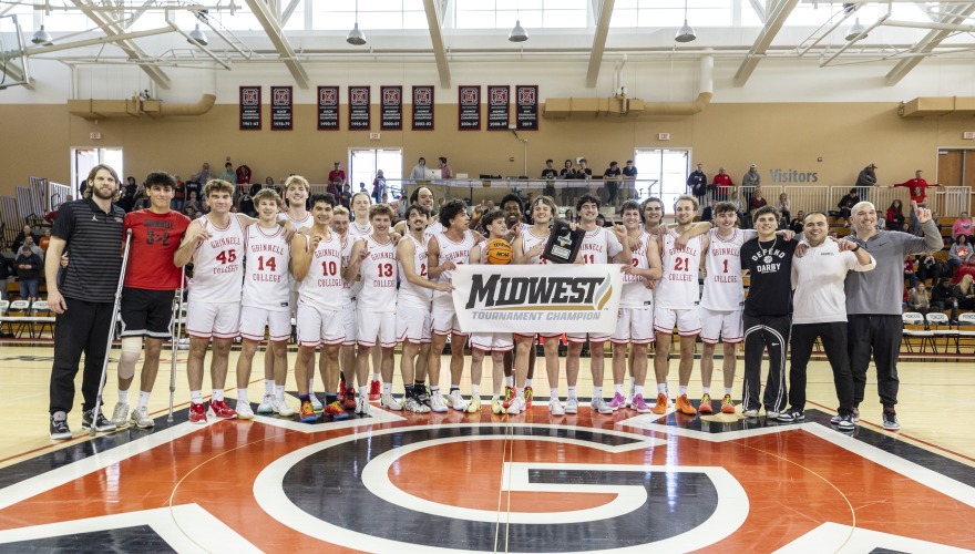 Men's basketball players wearing white uniforms holding a banner that reads "Midwest Tournament Champion"