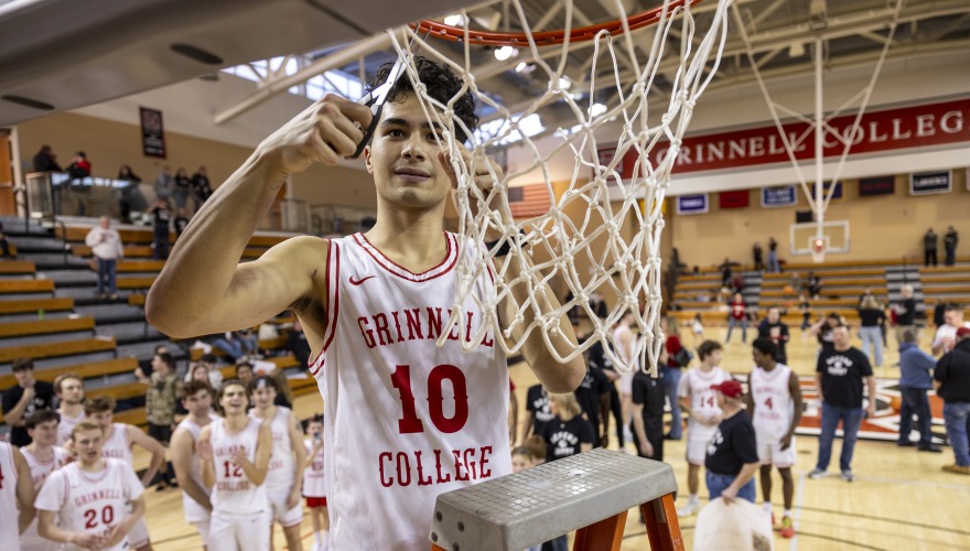 Grinnell basketball player, wearing a white number 10 jersey, cuts down the net
